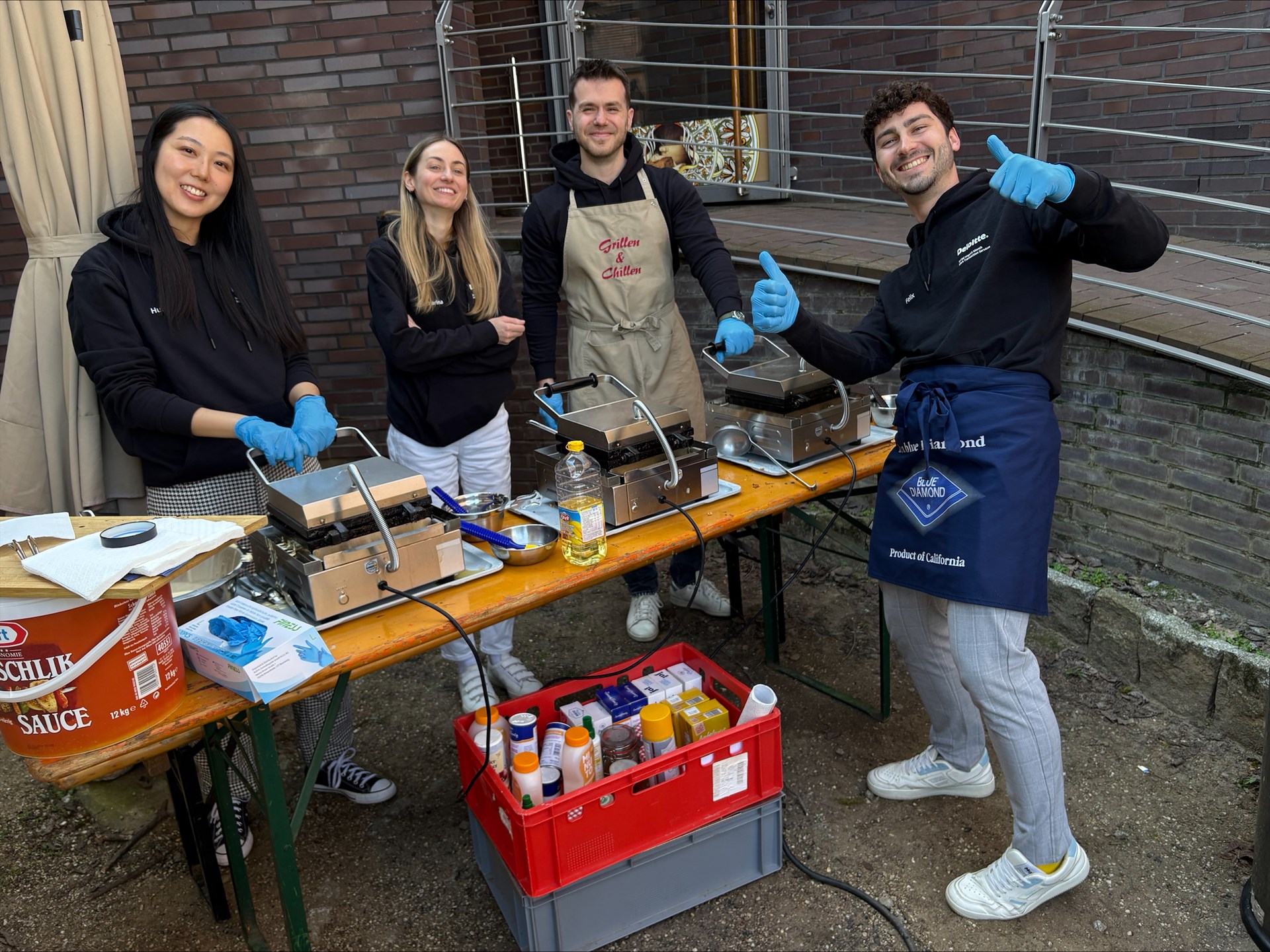 Vier Menschen lächeln in die Kamera und stehen an einem Tisch und bereiten Waffeln vor.