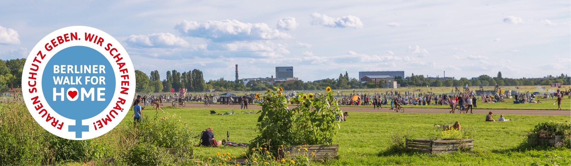 Ein Feld mit Sonnenblumen und vielen Menschen im Hintergrund. Links ist das Logo vom Berliner Walk for Home zu sehen.